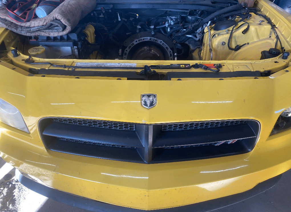 Yellow Dodge vehicle with hood open showing engine bay during repair work at RJ Fox Automotive