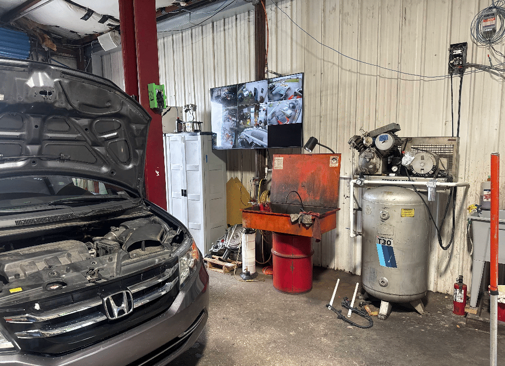 Auto repair bay with Honda on lift and security camera system monitoring work area
