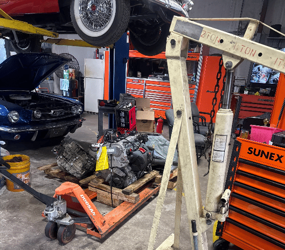 Engine and transmission removal setup with hoist in automotive repair shop bay